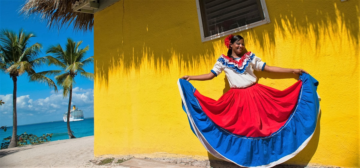 אשה בלבוש דומיניקני מסורתי רוקדת ליד בונגלו